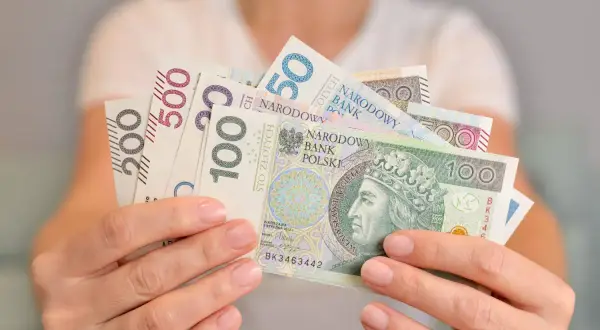 Dłonie trzymają polskie banknoty o nominałach 50, 100, 200 i 500 zł. Kto kontroluje fundusz socjalny w szkole?