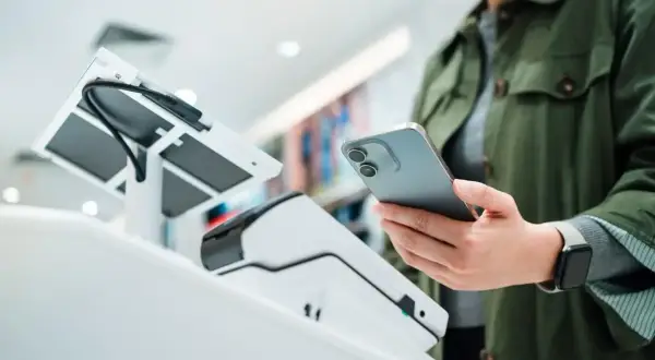 Kobieta zbliża telefon do terminala płatniczego, by spłacić pożyczkę w IKO.