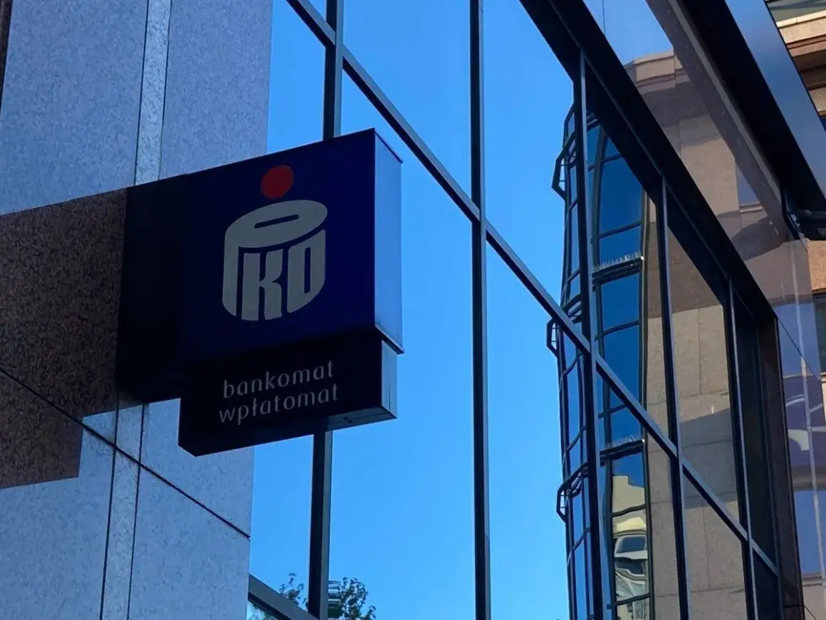Niebieski szyld PKO BP z napisem "bankomat wpłatomat" na tle szarej ściany i błękitnego nieba. To jak eliksir dla Twoich finansów.