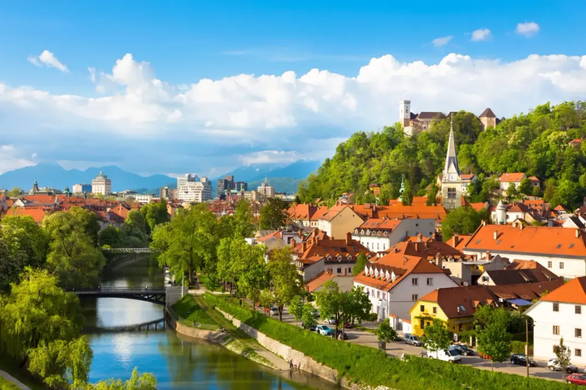 Widok na rzekę Ljubljanicę, most i miasto z zamkiem na wzgórzu w Słowenii.