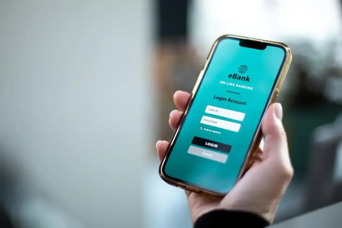 Dłoń trzyma smartfon z ekranem logowania do bankowości internetowej. Można tu wykonać przelewy wychodzące PKO BP.