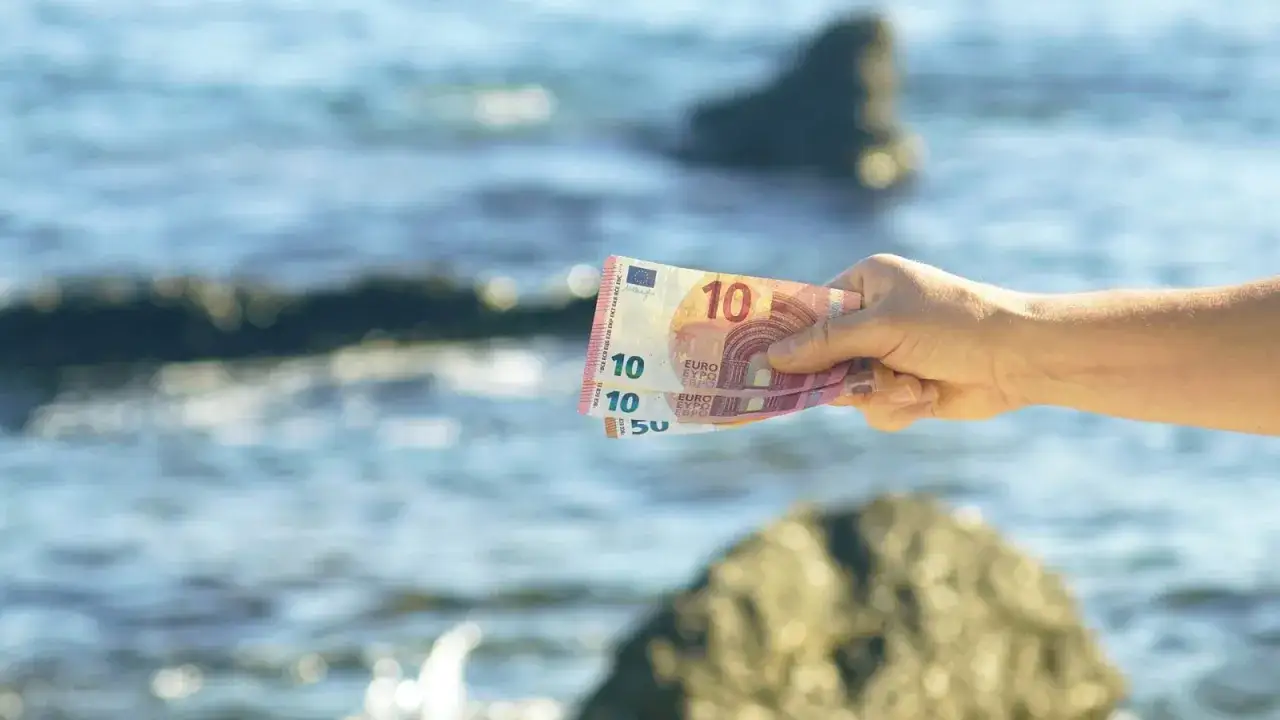 Dłoń trzyma banknoty euro na tle morza. W Czarnogórze obowiązuje euro, więc to idealna waluta na wakacje.