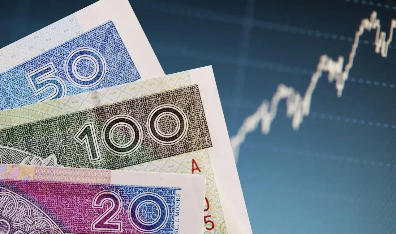 Polskie banknoty 50, 100 i 200 zł na tle wykresu giełdowego. Fundusz gwarancyjny chroni oszczędności w razie problem&oacute;w banku.