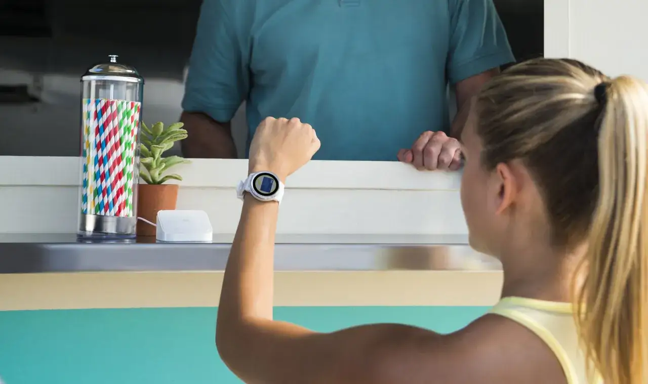 Kobieta zbliża zegarek z funkcją Garmin Pay do terminala płatniczego.