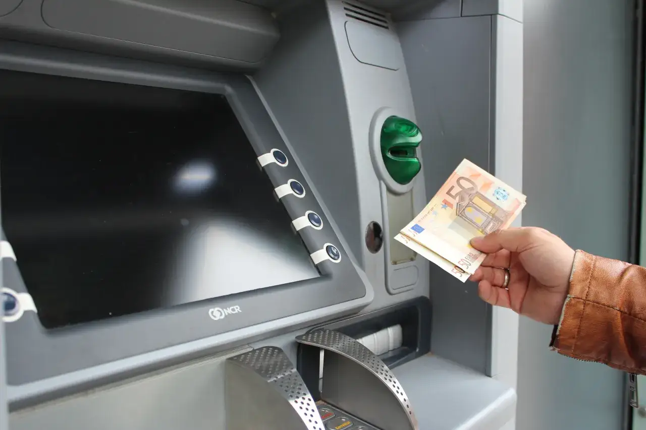 Ręka trzyma banknoty 50 euro przy bankomacie. W Grecji obowiązuje euro, więc to typowa waluta.