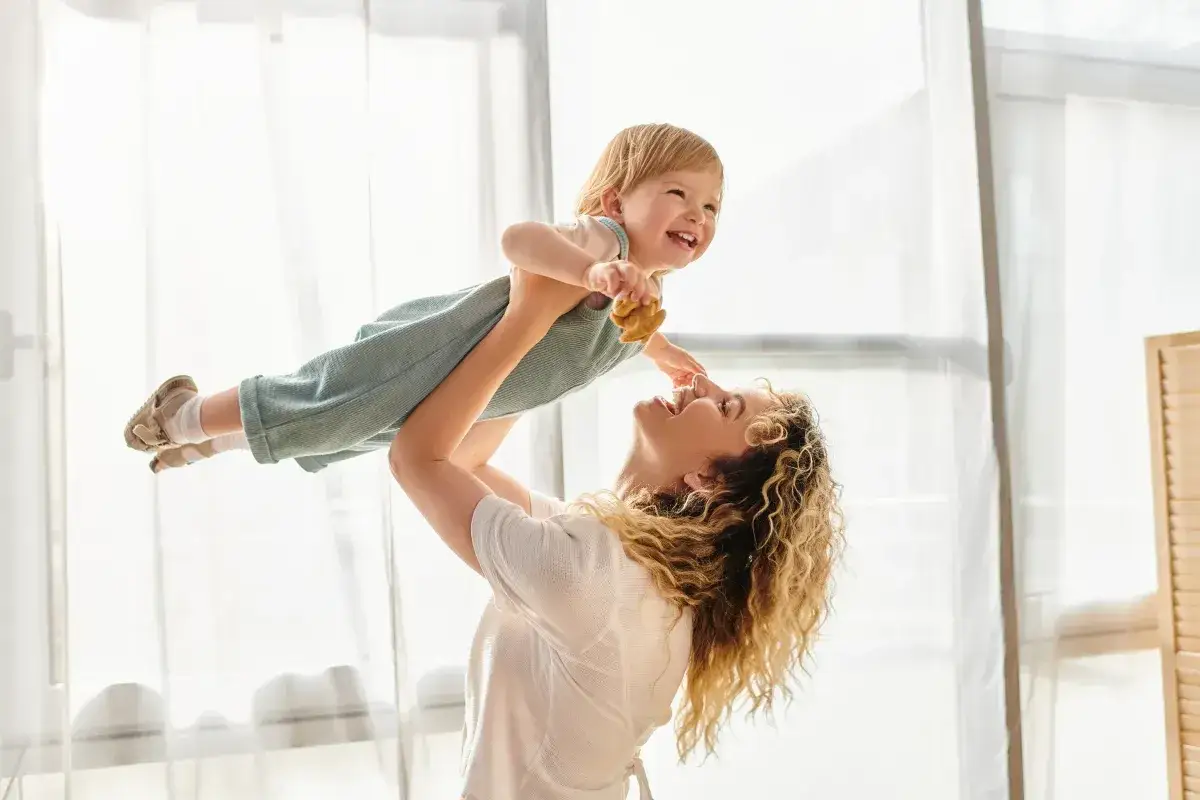 Szczęśliwa mama podrzuca dziecko. Dofinansowanie do żłobka może pomóc w opiece nad maluchem.