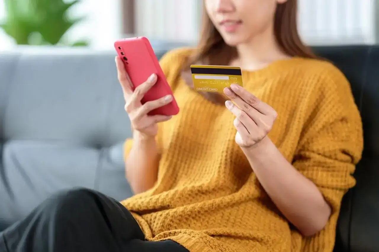 Kobieta trzyma telefon i kartę, szukając informacji, jak odblokować kartę Santander.