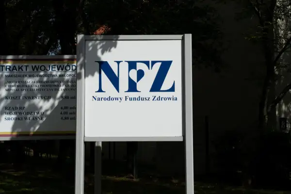 Tablica z logo NFZ i napisem Narodowy Fundusz Zdrowia. Obok tablica z informacjami o inwestycji w szpital.