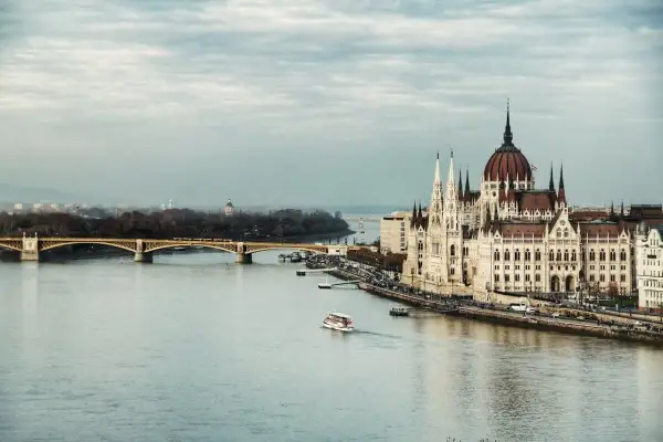 Budynek Parlamentu w Budapeszcie nad Dunajem. W tle most i panorama miasta. Pytanie: jaka jest waluta w Budapeszcie? Odpowiedź: Forint.