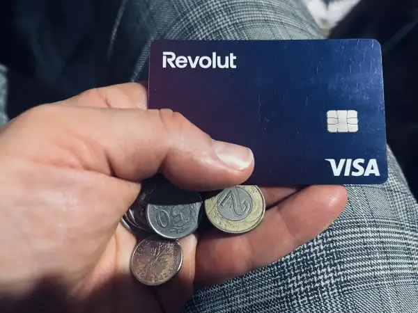 Dłoń trzyma kartę Revolut i polskie monety. Kto jest właścicielem Revolut? To pytanie, na które odpowiedź znajdziesz w aplikacji.
