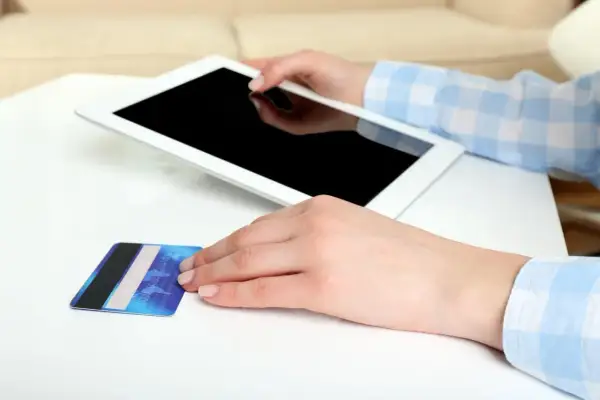 Dłonie trzymają tablet i kartę płatniczą. Zastanawiasz się, jak aktywować BLIK w Millenium?
