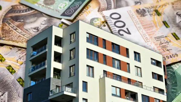 Nowoczesny budynek mieszkalny na tle polskich banknotów. Zastanawiasz się, ile obecnie wynosi oprocentowanie kredytu hipotecznego?