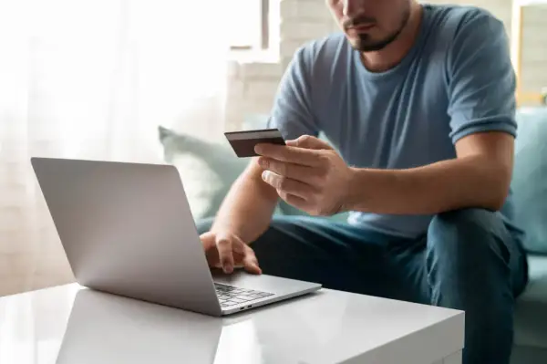 Mężczyzna z kartą kredytową przed laptopem, uczący się, jak założyć PayPal.