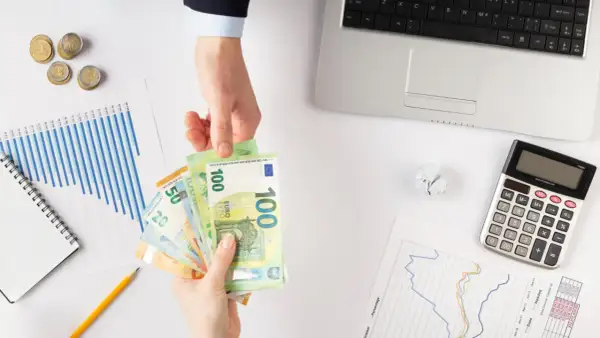 Ręce przekazują sobie euro. Obok leżą wykresy, kalkulator i monety. Zastanawiasz się, jaki podatek od pożyczki?