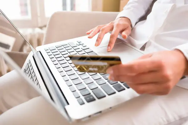 Kobieta z kartą płatniczą wpisuje kod BIC na laptopie, realizując płatność online.