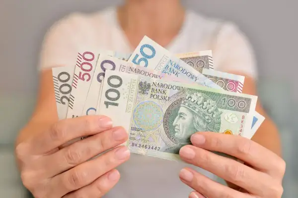 Dłonie trzymają polskie banknoty o nominałach 50, 100, 200 i 500 zł. Kto kontroluje fundusz socjalny w szkole?